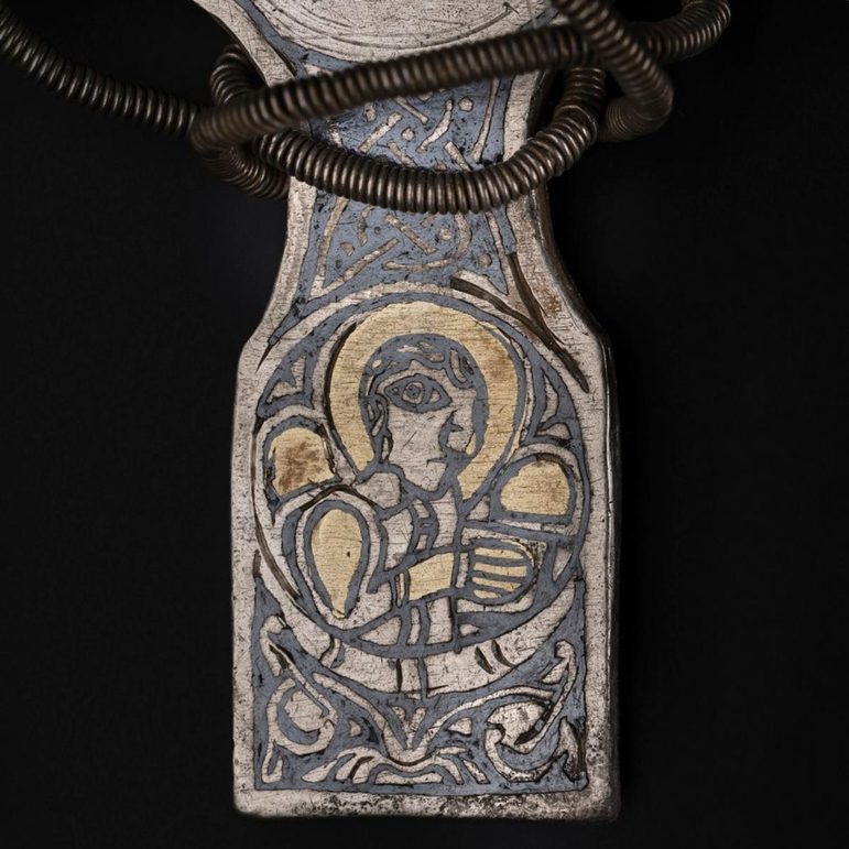 A part of a cross pendant showing the lower arm. A saint is depicted with a gold halo.