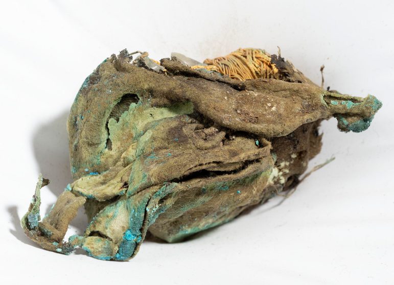 A small portion of gold on an object laid on its side peeks out beneath green-stained fabric wrapping.