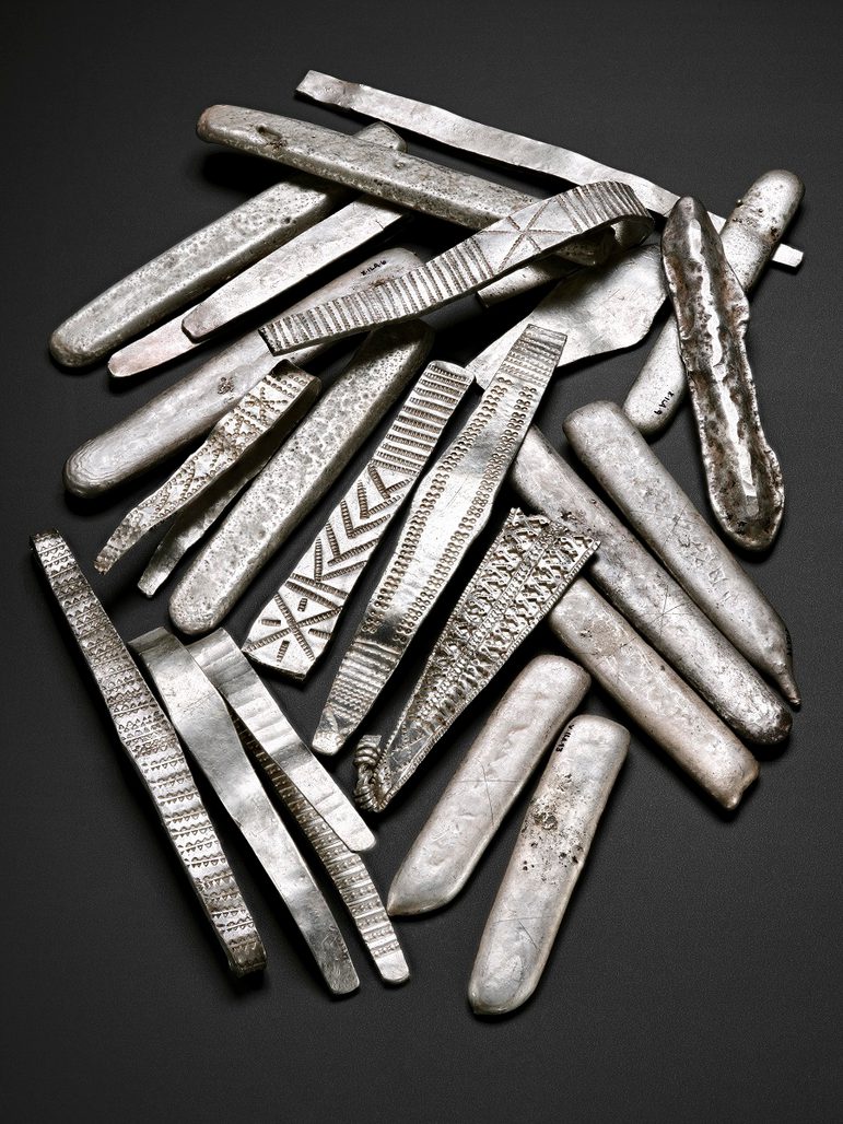 A group of flat long pieces of silver with various different details and inscriptions.