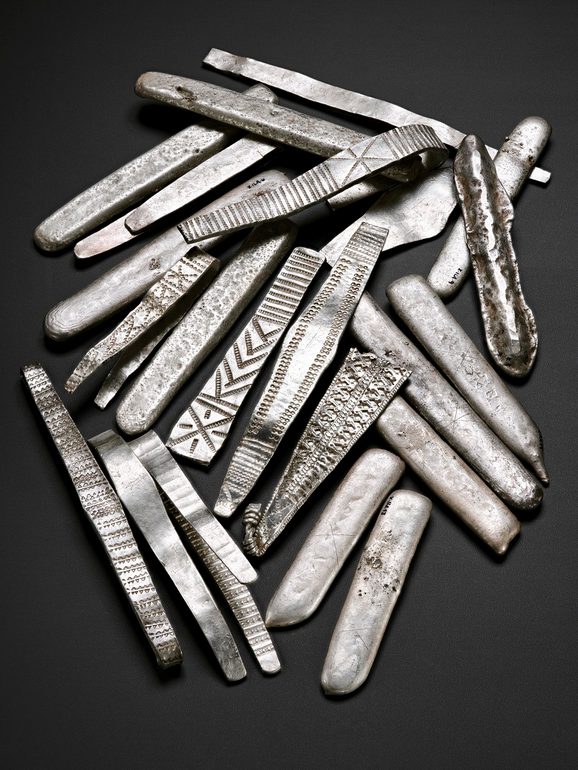 A group of flat long pieces of silver with various different details and inscriptions.