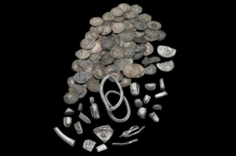 A large group of tarnished silver coins and other fragments of silver objects arranged on a black background