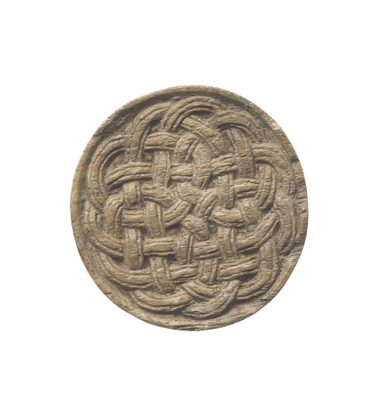 A beige stone in the shape of a disk with a knotted celtic pattern
