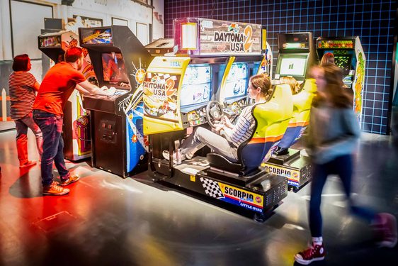 A group of people playing different arcade games in the Game On exhibition.