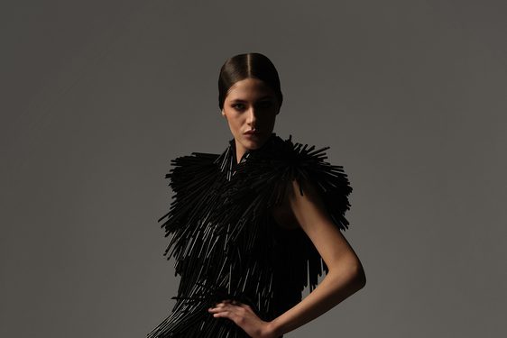 A model posing in a dress composed of black straws.