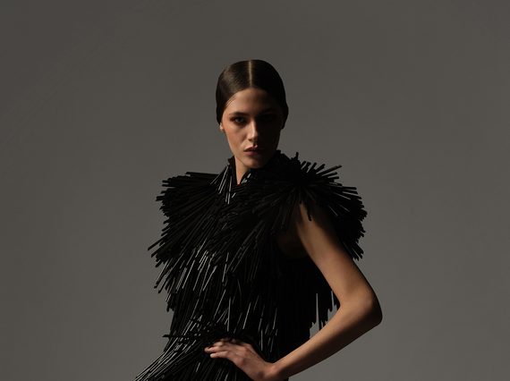 A model posing in a dress composed of black straws.