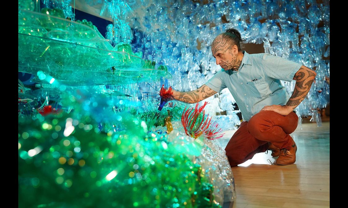 Artist George Nuku arranging the of installation of "Bottled Ocean 2123". George is surrounded by plastic bottles that have been cut and modelled to represent the wildlife of the ocean.