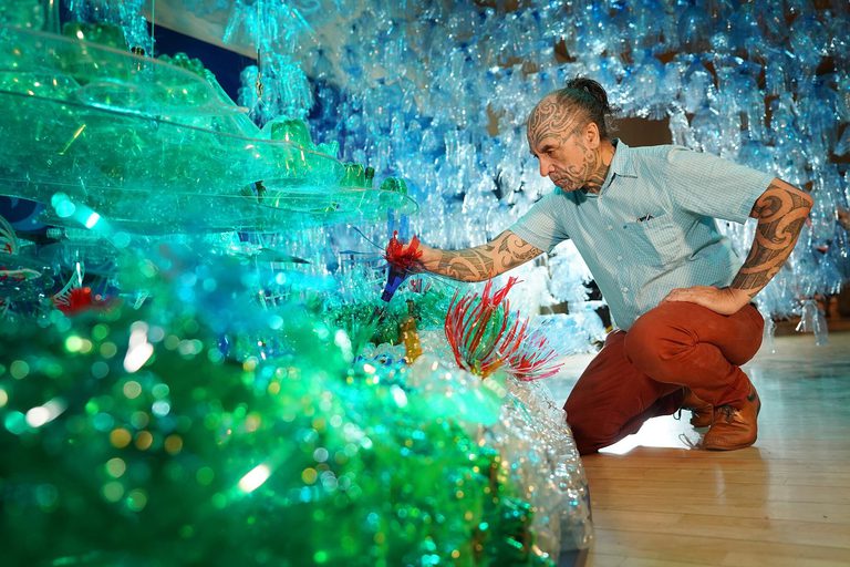 Artist George Nuku arranging the of installation of "Bottled Ocean 2123". George is surrounded by plastic bottles that have been cut and modelled to represent the wildlife of the ocean.