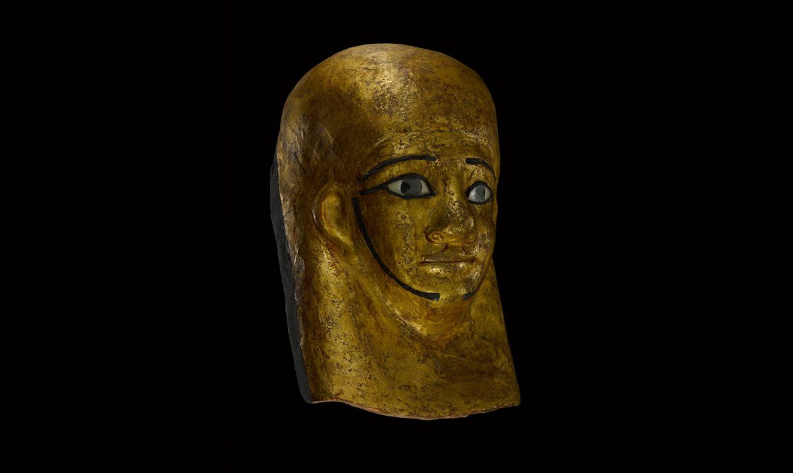 An Egyptian gold funerary mask of a person's face with painted eyes and eyebrows