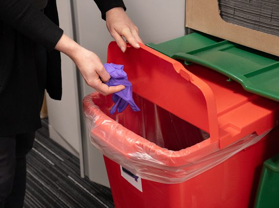 A conservator putting a pair of nitrile gloves into a red recycling box.