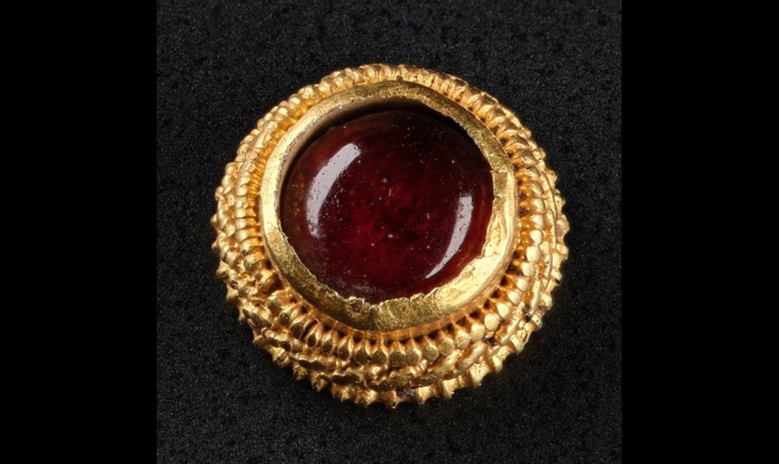 A piece of jewellery with a round red stone surrounded by detailed gold rings