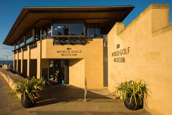 The exterior of a modern museum building constructed of orange-yellow stone, the World Golf Museum.