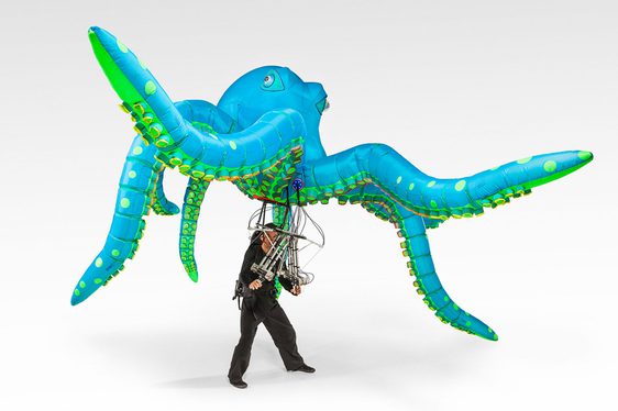 A person controlling a large inflatable illuminated octopus puppet.