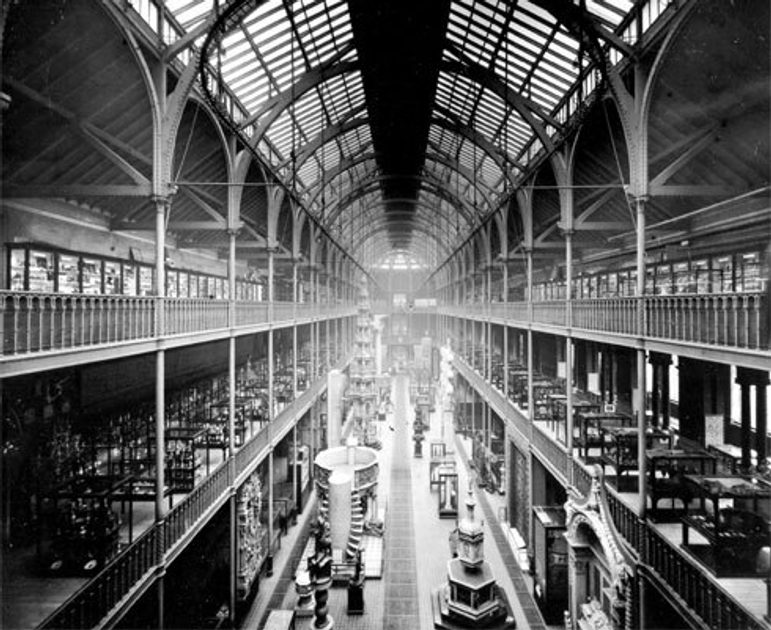 A black and white photograph of a long museum hall with a high arched roof and three floors