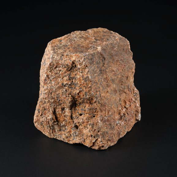 A piece of pink granite with flecks of grey, black and brown against a black background.