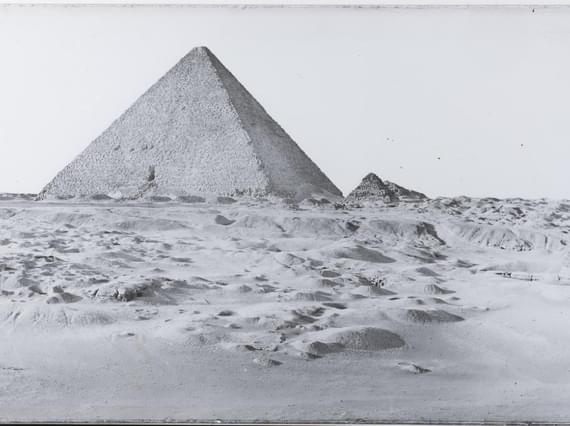 A black and white image of a pyramid in a sandy landscape. There is a yellowing label to the left of the image with handwritten notes scrawled on it.