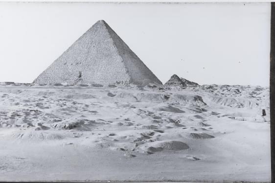 A black and white image of a pyramid in a sandy landscape. There is a yellowing label to the left of the image with handwritten notes scrawled on it.