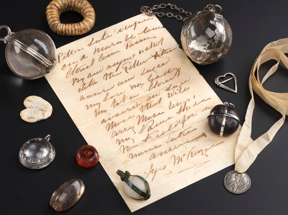 Parchment paper with writing, surrounded by 11 jewels, beads and metal objects used as medical charms