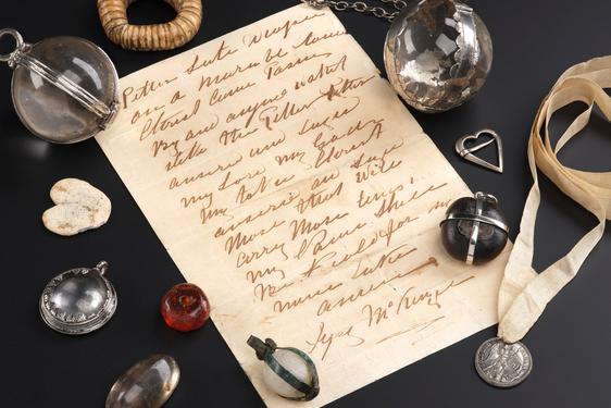 Parchment paper with writing, surrounded by 11 jewels, beads and metal objects used as medical charms