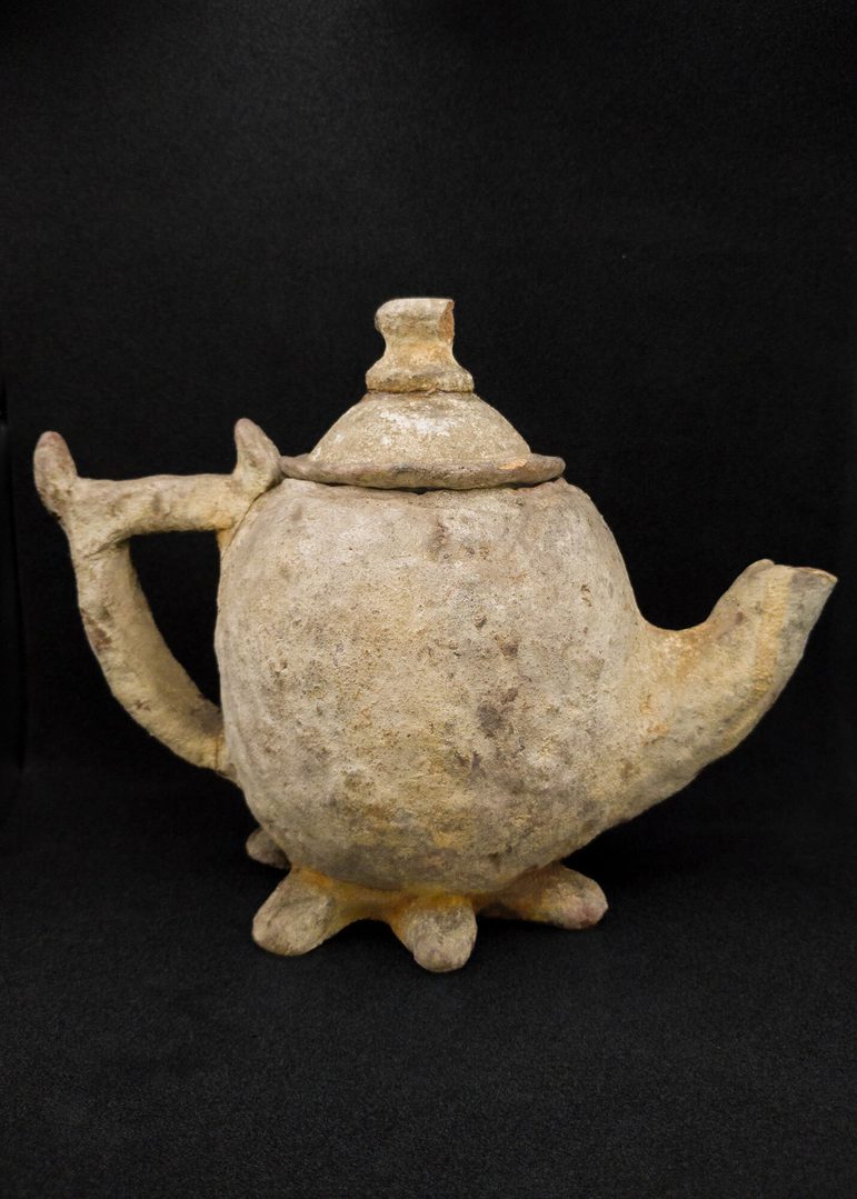 A teapot of unglazed earthenware with a large handle and deeply serrated foot.