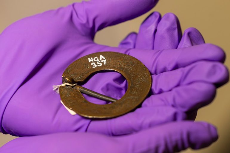 A small copper ring brooch with letters engraved on it.