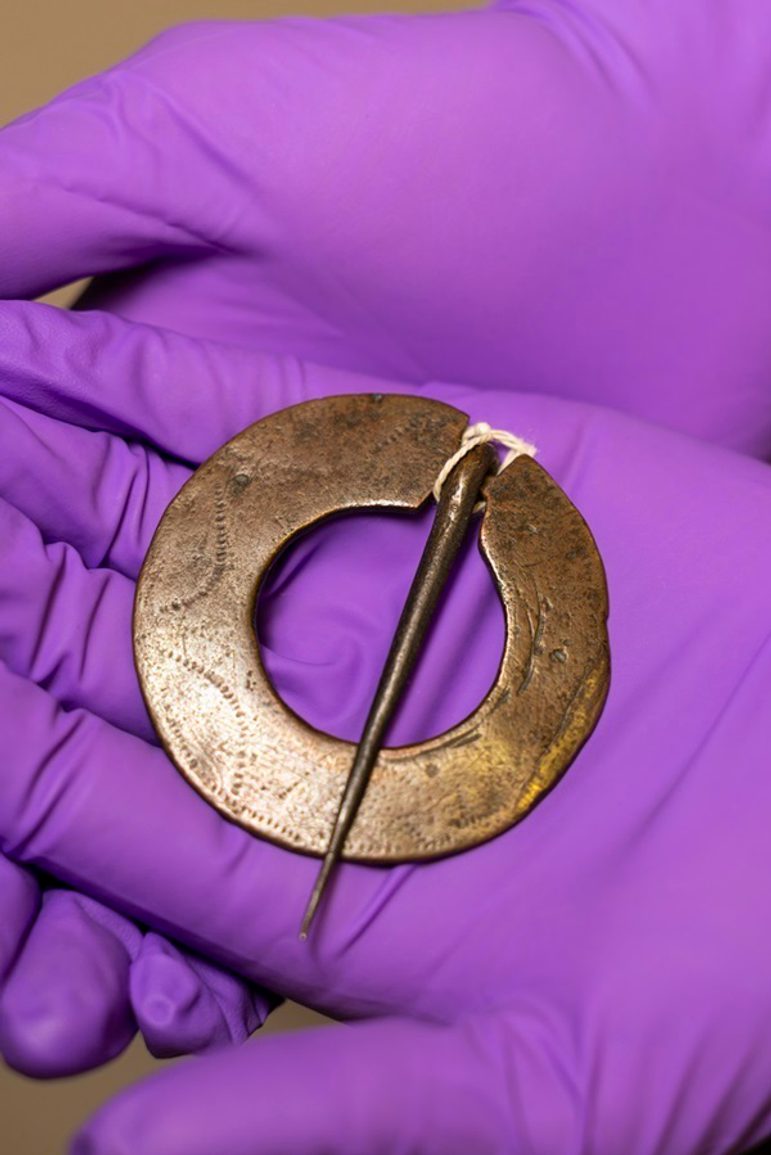A small copper ring brooch with letters engraved on it.