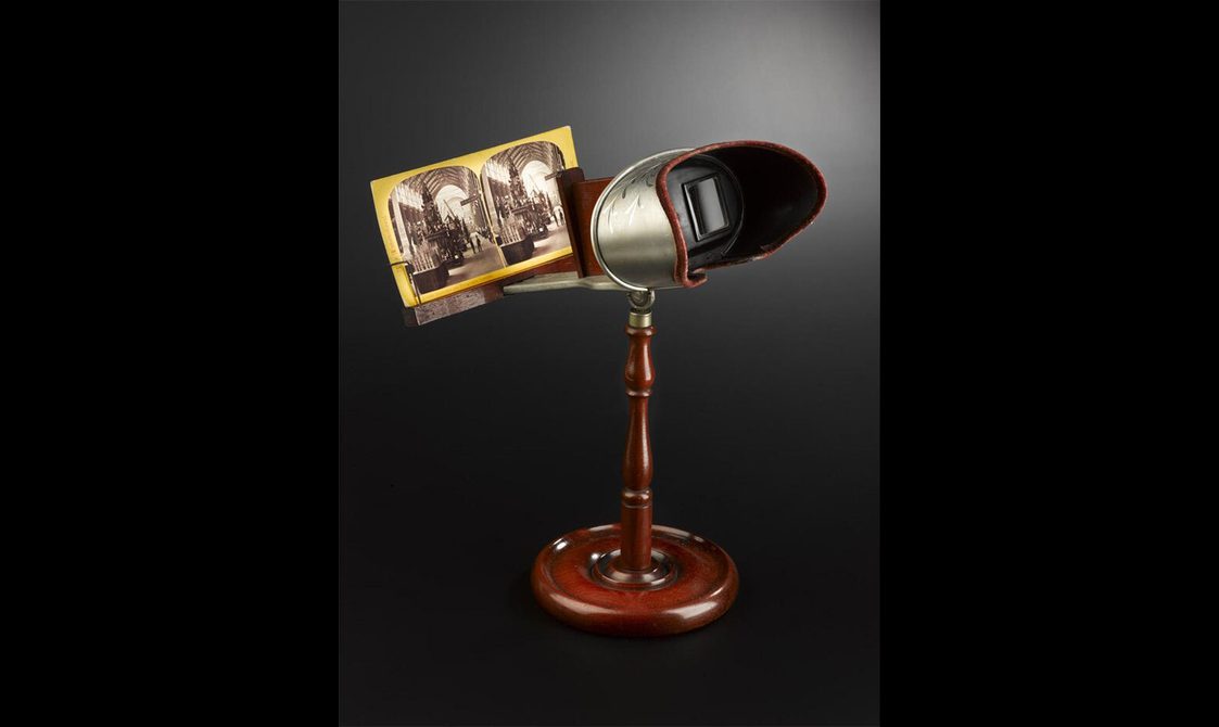 A set of lenses on a wooden stand with a double photograph held in front of the lenses.