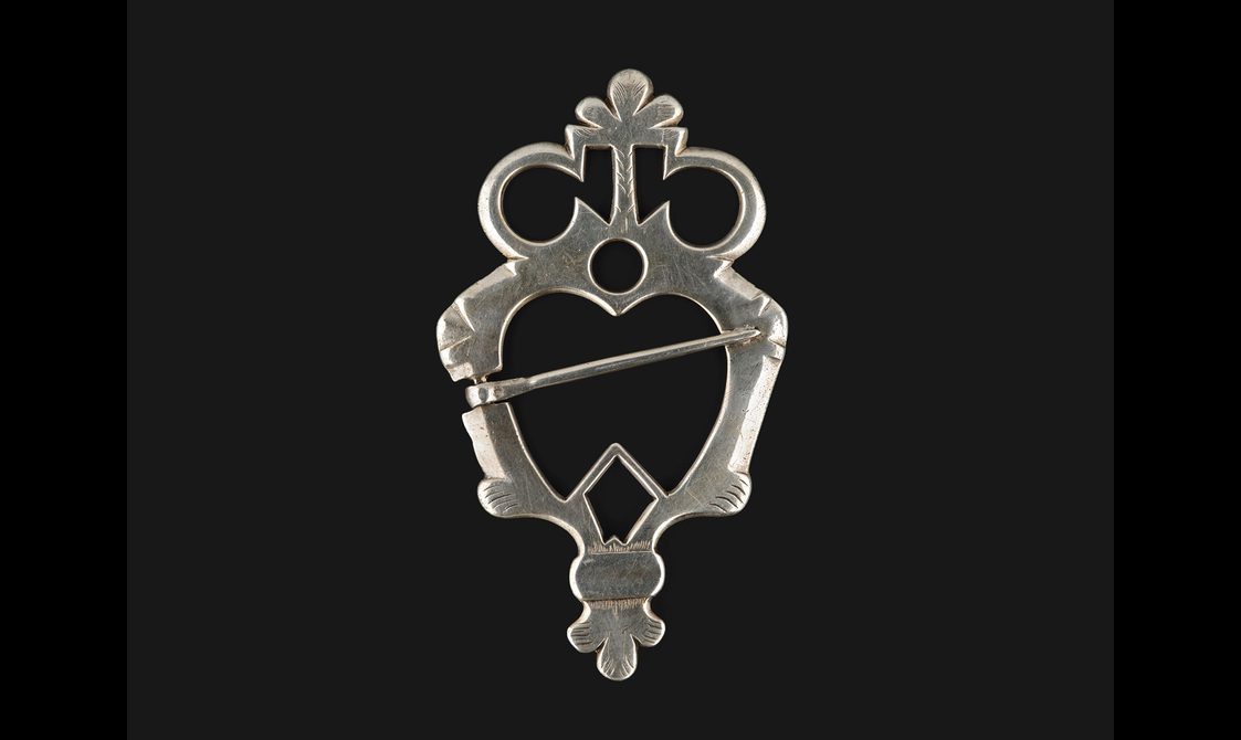 A silver heart shaped brooch with a crown on top