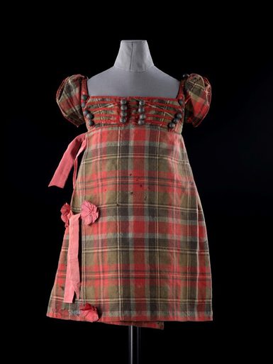 A mannequin wearing a red tartan dress with an empire waist and capped puff sleeves.