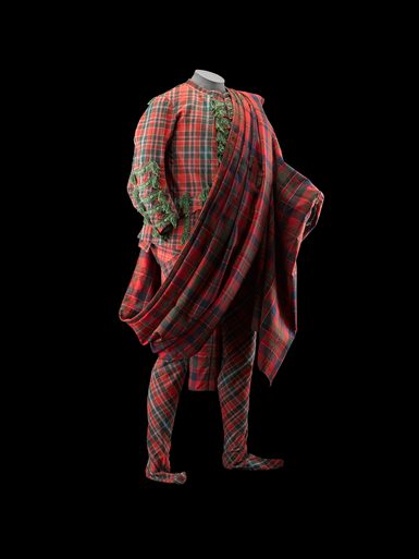 A mannequin wearing red tartan jacket and trousers with a shawl draped diagonally across the body.