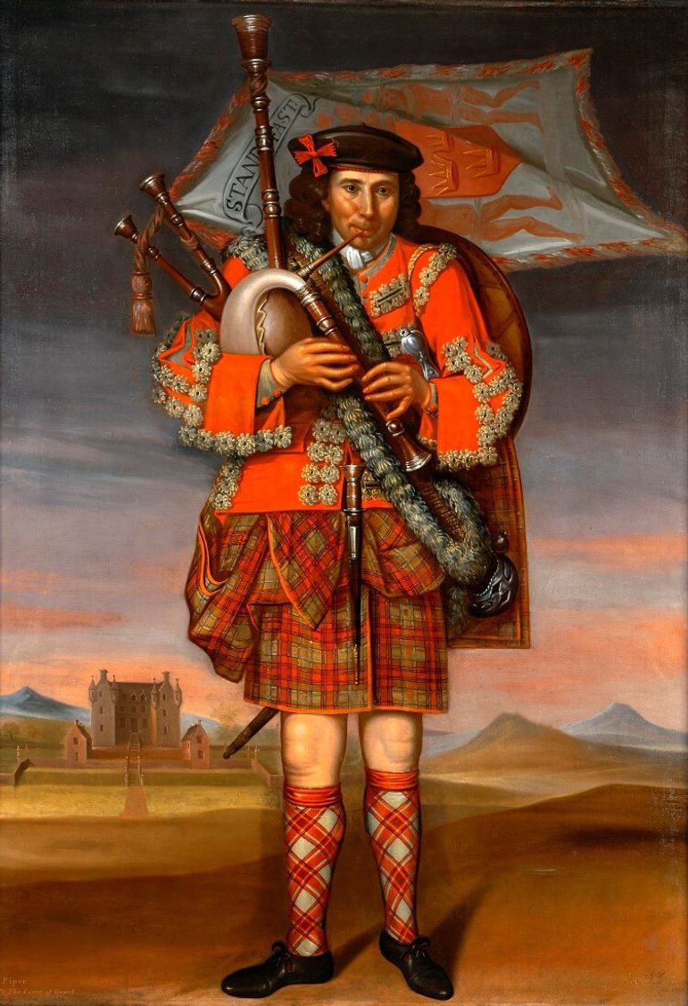 Bagpiper in bright red, billowing tartan uniform with a banner flying from the pipes. He stands in a rural setting with a castle behind him.