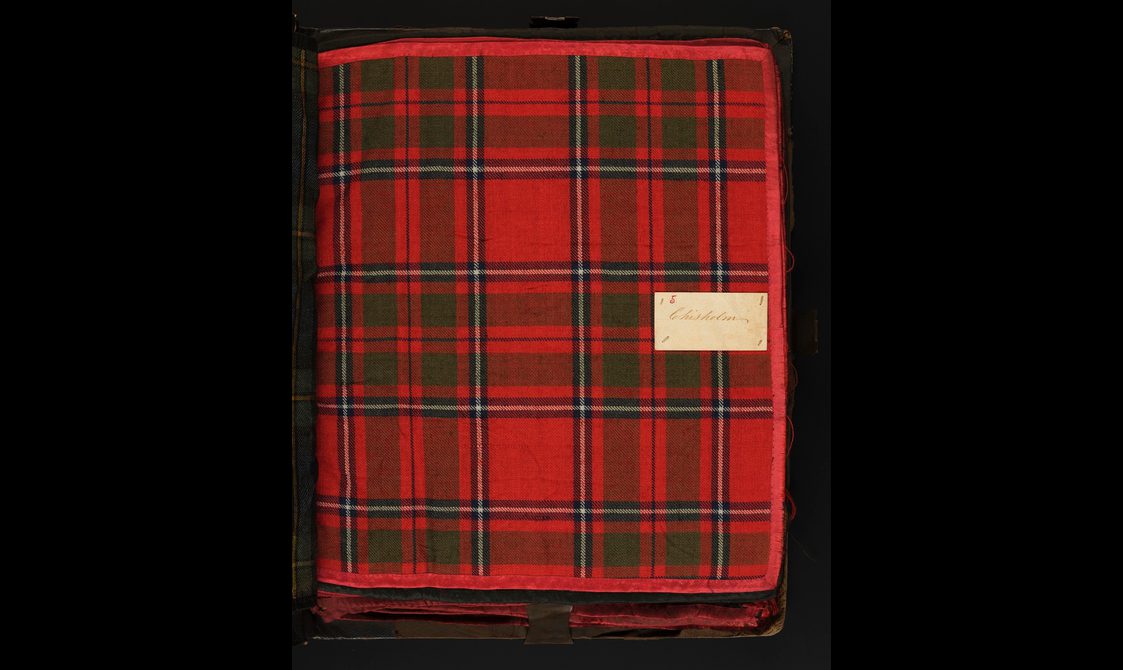 A swatch of a red checked tartan fabric with a label sewn to the right.