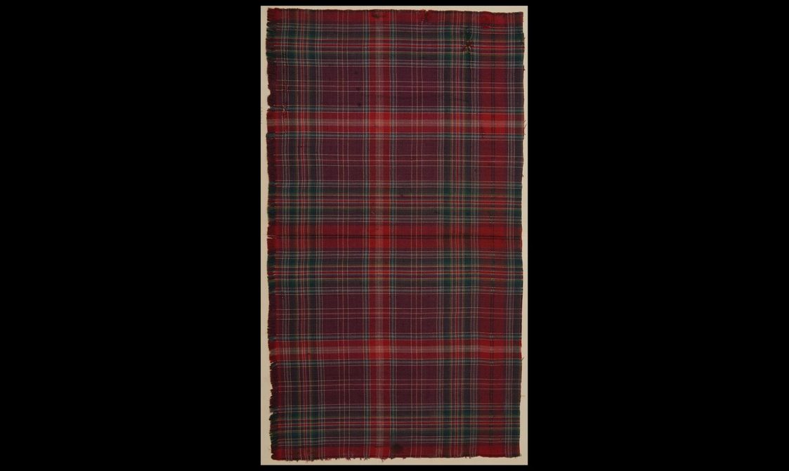 Tall rectangular swatch of burgundy, dark blue, red and light green tartan fabric against a black background.
