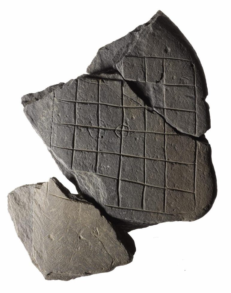 A large piece of rock with a grid etched into its surface. A smaller piece of rock is beside it.