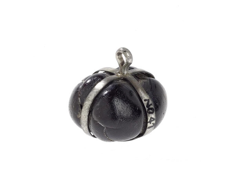 Dark brown seed mounted in silver bands. There is a small silver hoop for a chain at the top of the strips.