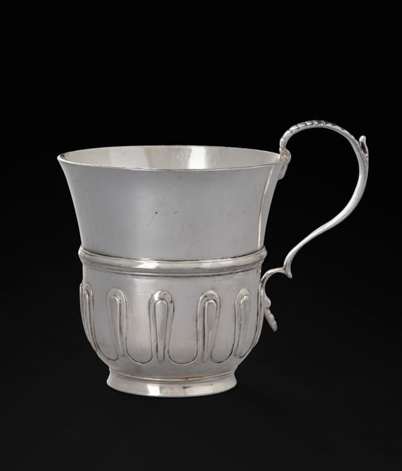A silver cup with a looped design at the bottom and a thin cup handle