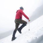 A man in a red jacket and hat hiking up a snowy mountain.