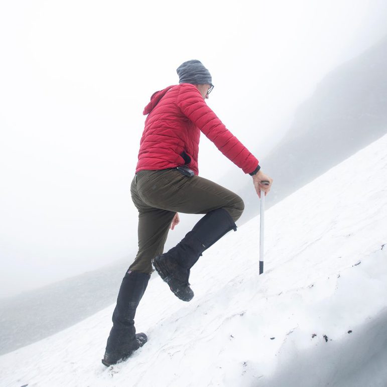 A man in a red jacket and hat hiking up a snowy mountain.
