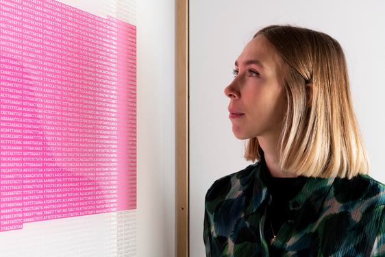 A person is looking at a framed picture. The picture looks like a square block of pink from a distance, but on closer inspection it's a stream of code for a virus.