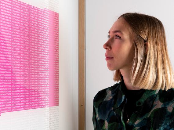 A person is looking at a framed picture. The picture looks like a square block of pink from a distance, but on closer inspection it's a stream of code for a virus.