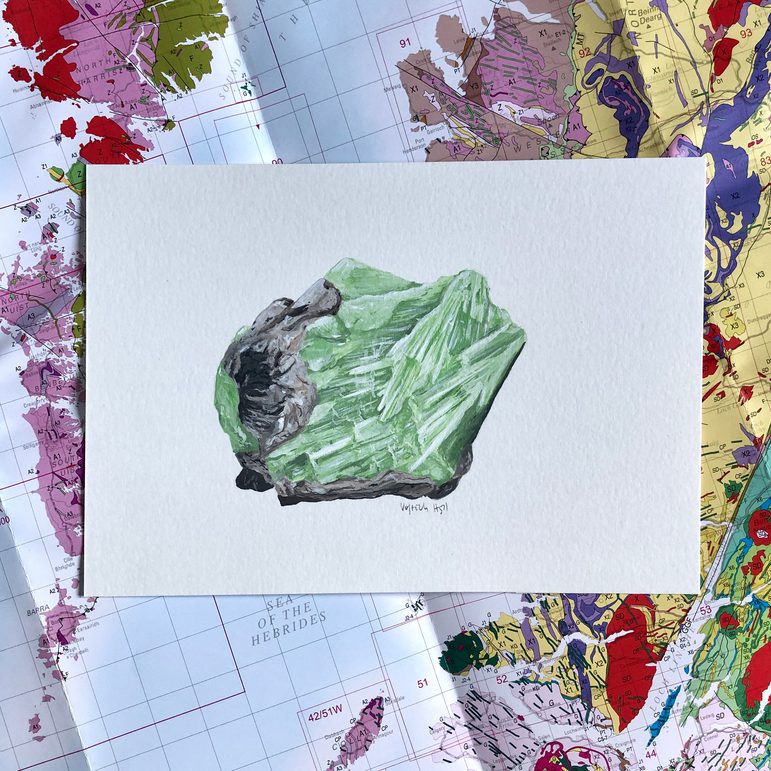 An illustration of a green mineral on a white piece of paper. The illustration is photographed against a geological map of Scotland.