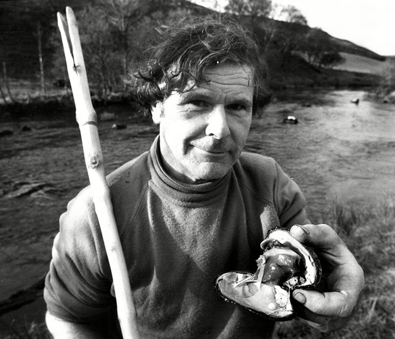 Black and white image of fisherman holding a mussel fishing stick and open mussel shell with a pearl.