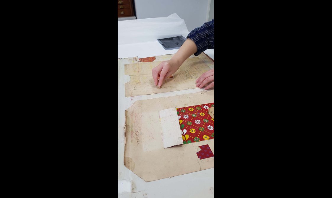 A piece of paper, which features an ornate pattern at its centre, is conserved by a conservator. Only the conservators hands are in shot.