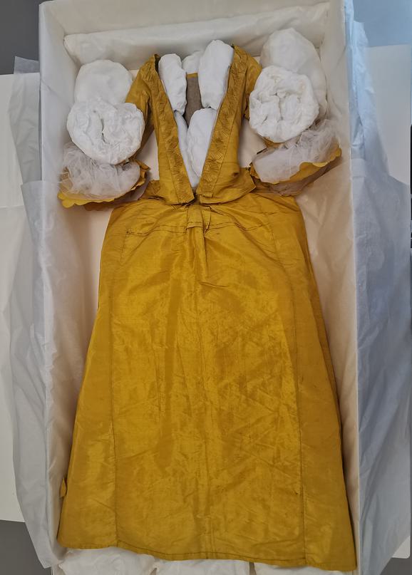 A yellow dress is padded with paper and packed into a box