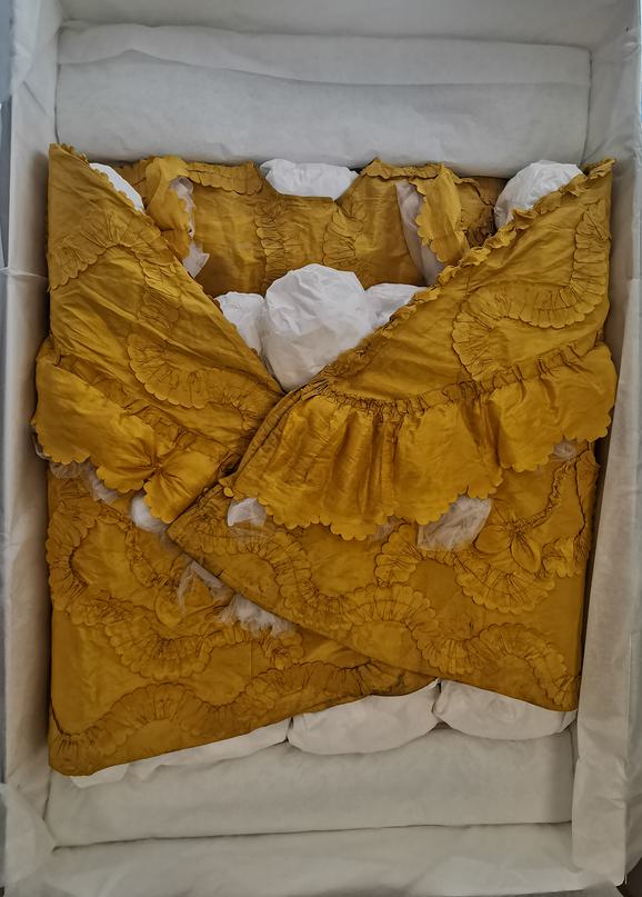 An ornate yellow garment is packed into a box