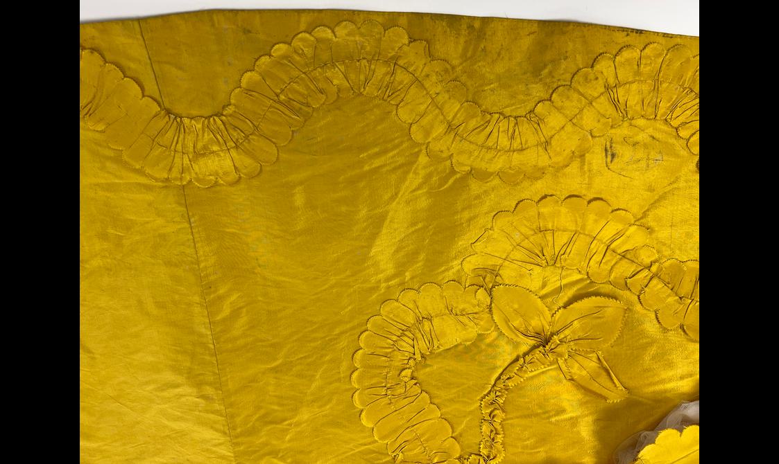 A close of up ornate scalloped edges stitched into a yellow garment