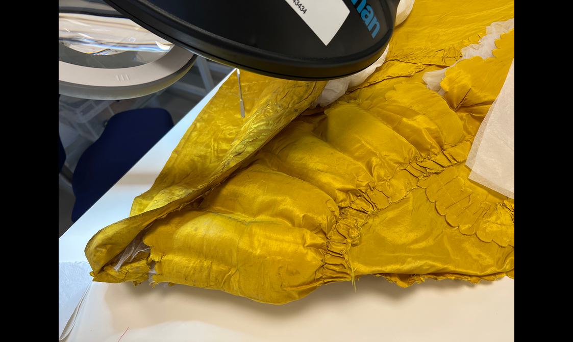 A yellow garment is inspected by a conservator