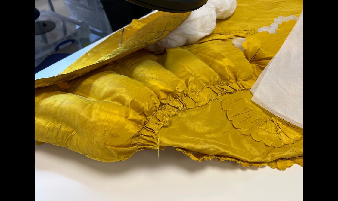 A close up view of the hem and seams of an ornate yellow garment