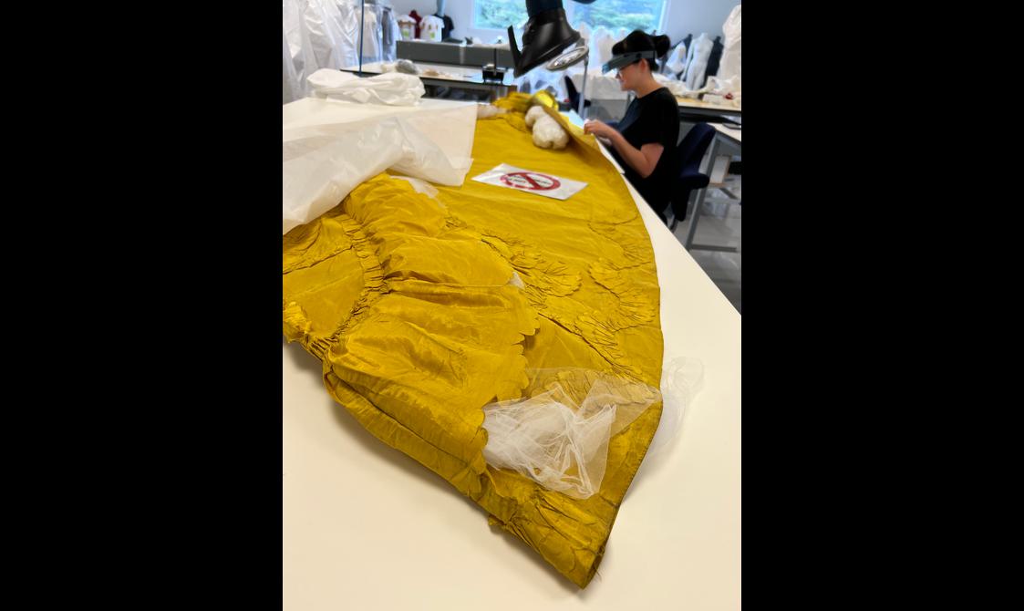 A yellow garment showing signs of damage is being conserved