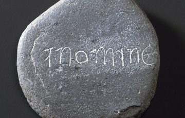 A flat grey stone with a carving in the surface that says 'in nomine'