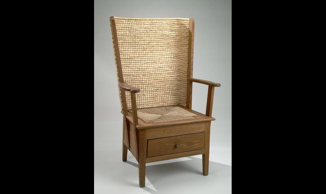 A wooden chair with a thatched back and drawer in the seat.